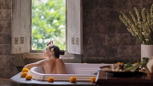 A bathtub with a view of greenery outside, a potted plant, and a decorative plate on the side. - The Jayakarta Bali (Legian)