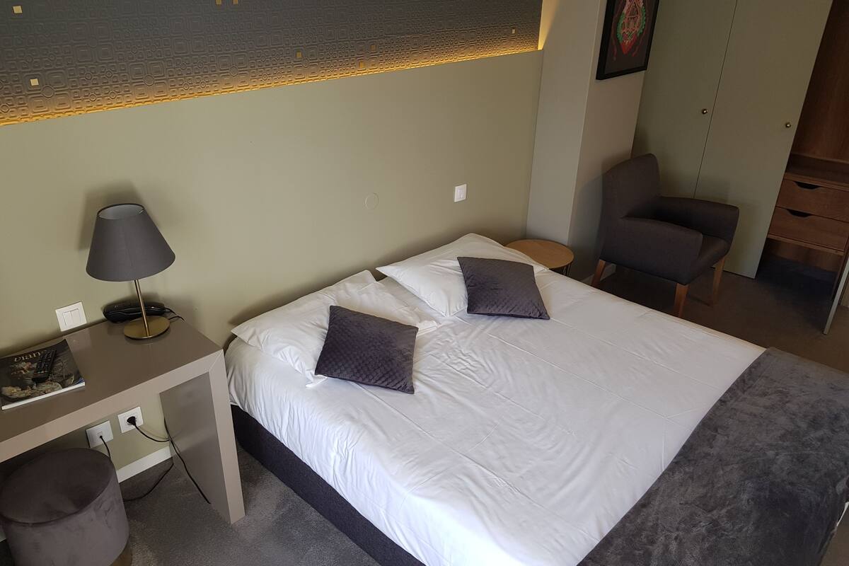 A neatly arranged bedroom with a bed, bedside table, lamp, chair, and desk.