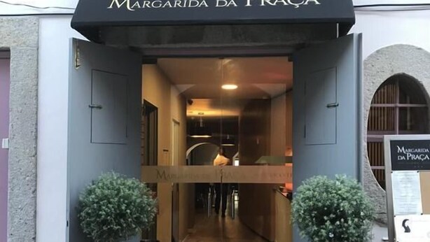 La entrada a Margarida da Praga, con un toldo negro, suelo de baldosas y dos plantas en macetas.
