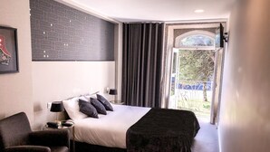 Habitación de hotel con una cama, una silla, una mesita de noche, una lámpara y vistas al exterior.