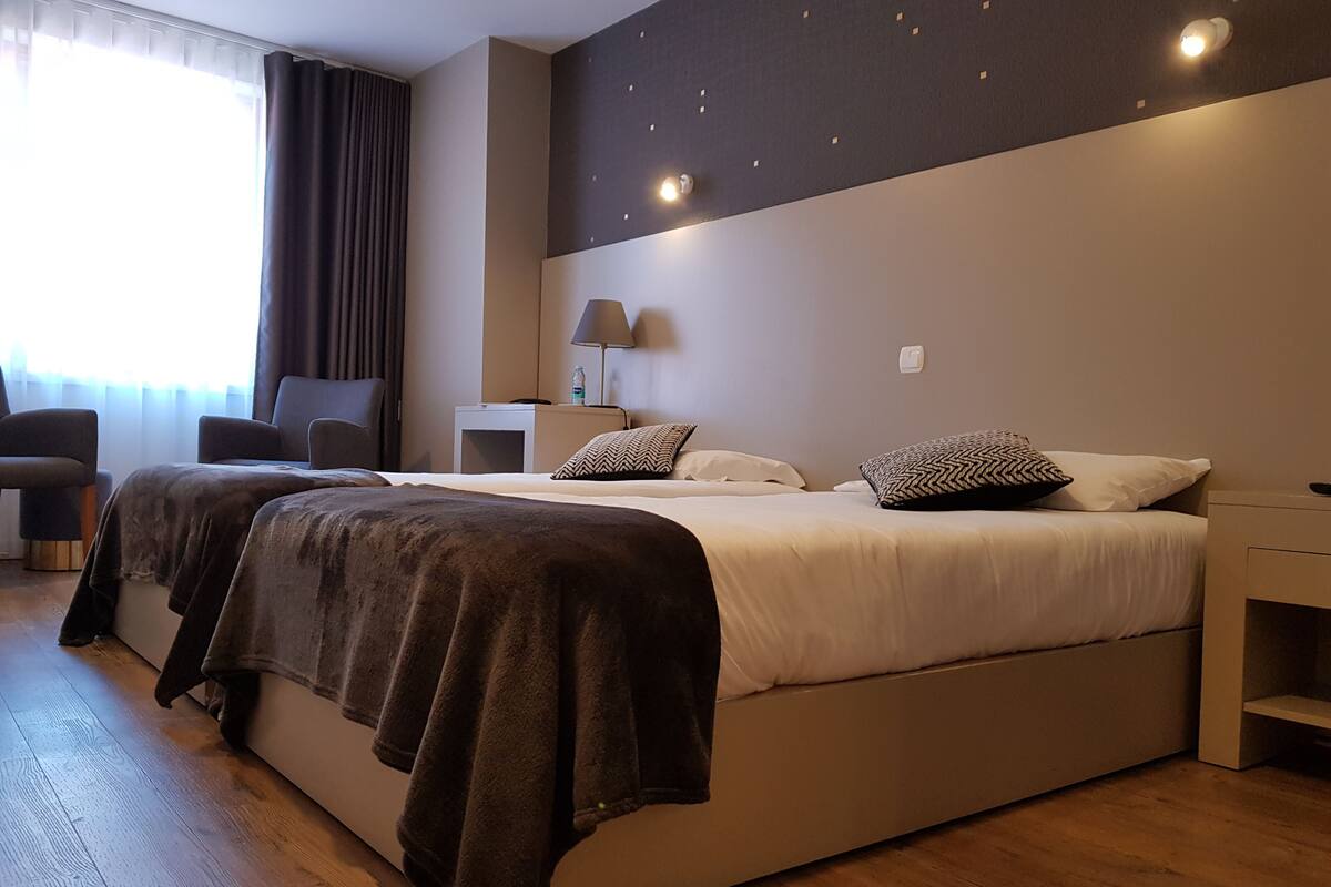 A modern hotel room with a large bed, a bedside table, a lamp, and a chair.