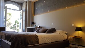 Un dormitorio moderno con una cama grande, mesitas de noche, una lámpara y vistas al verdor exterior.