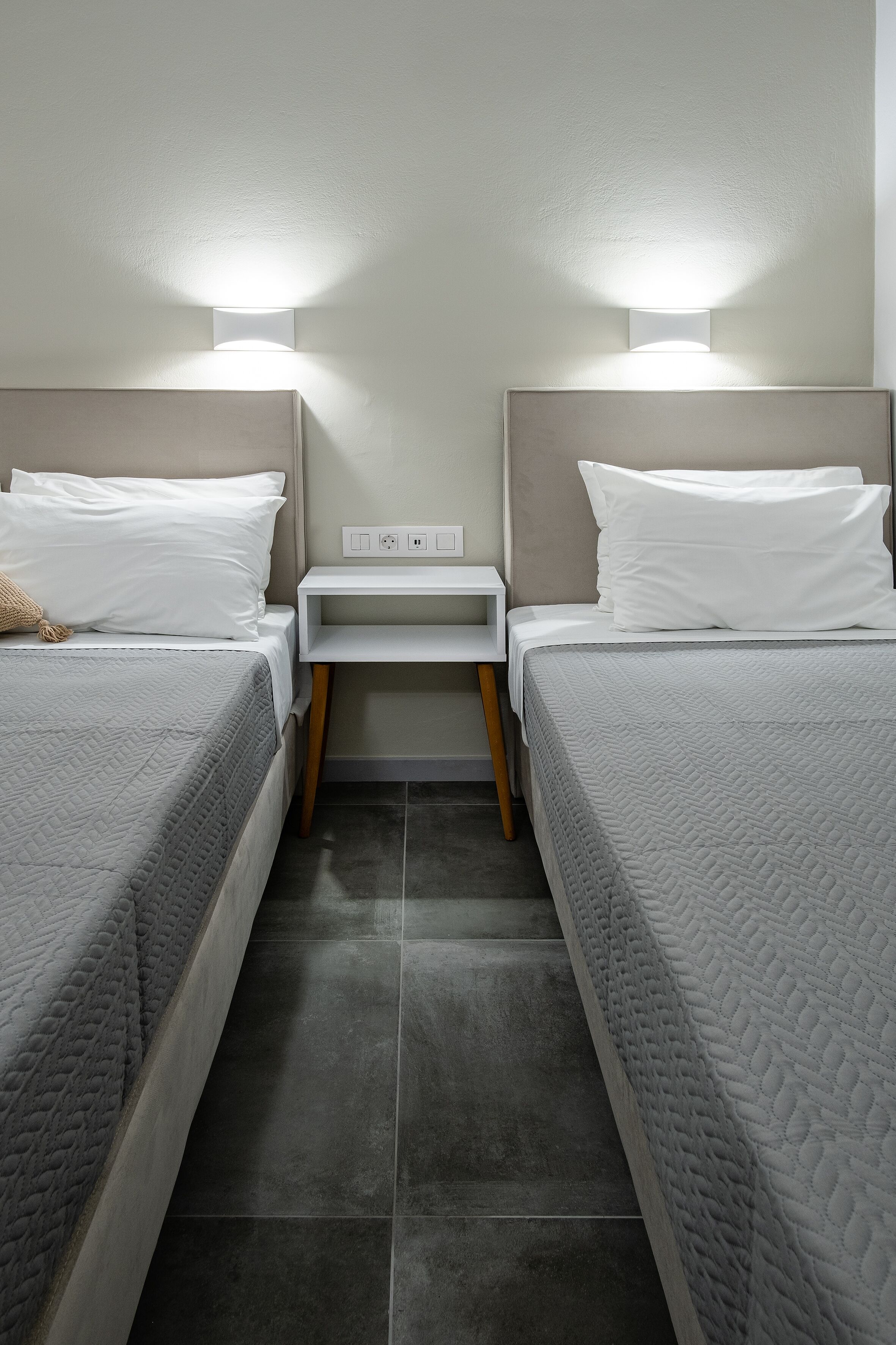 A twin room with two beds, a nightstand, and a wall-mounted light fixture.
