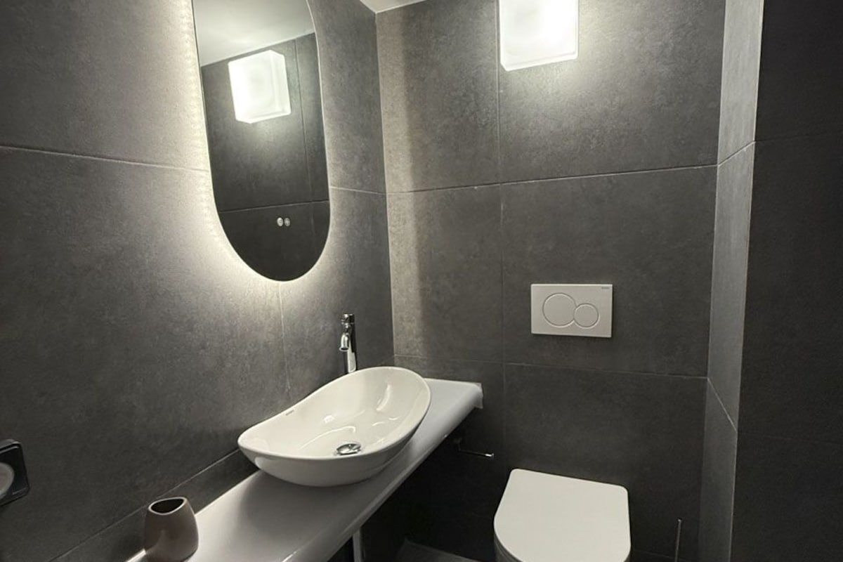 A modern bathroom with a white sink, a toilet, and a mirror.
