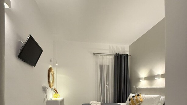 A modern hotel room with two beds, a flat-screen TV mounted on the wall, a small desk with a lamp, and a bathroom with a shower curtain.