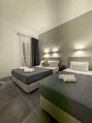 A hotel room with two beds, grey bedding, a small table with a phone, and a window with curtains. - Dilion Hotel (Paros)
