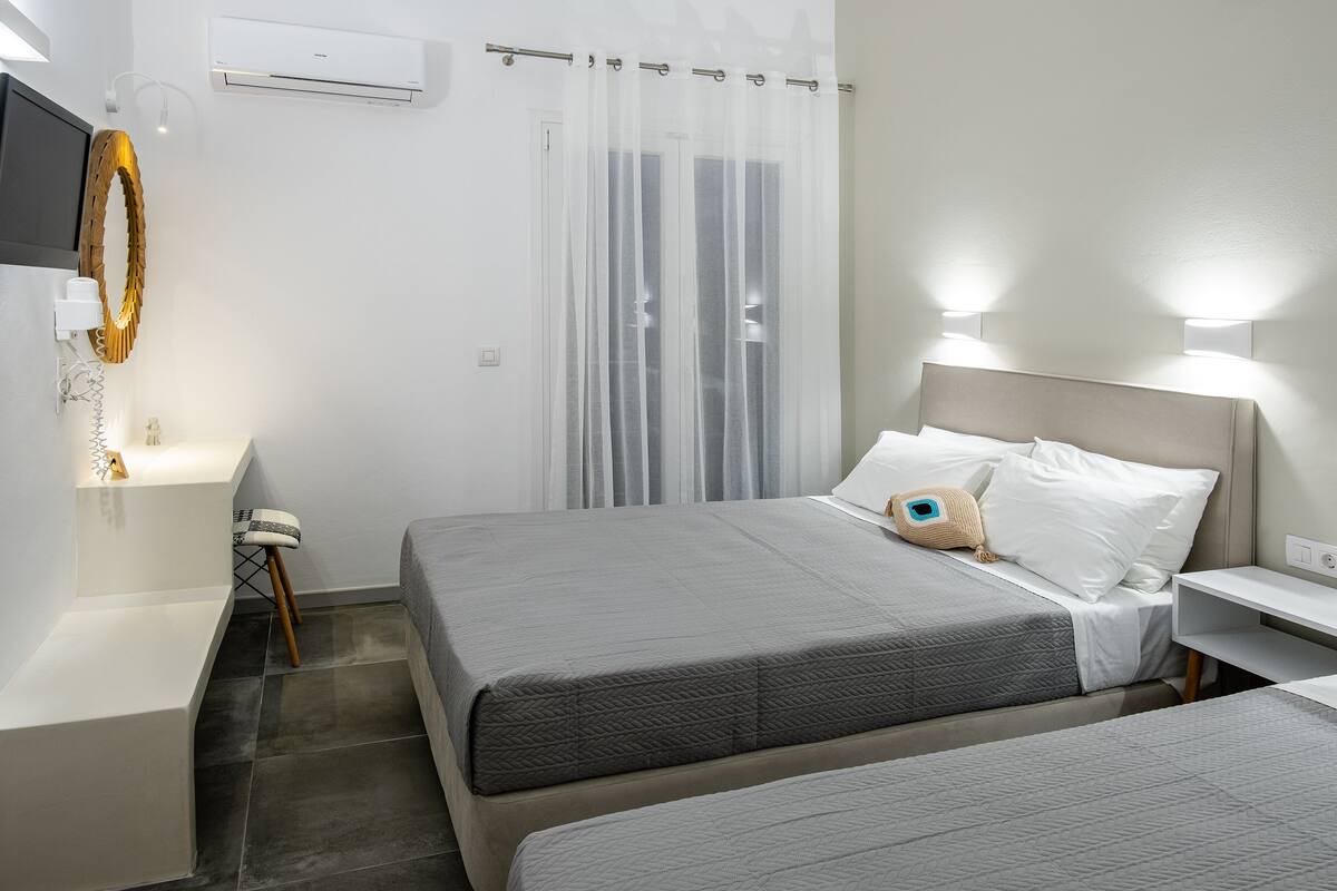 A hotel room with two beds, a bedside table, a chair, a TV, and a curtain.