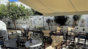 An outdoor patio with round tables and chairs, surrounded by white walls with circular cutouts and a patterned floor.