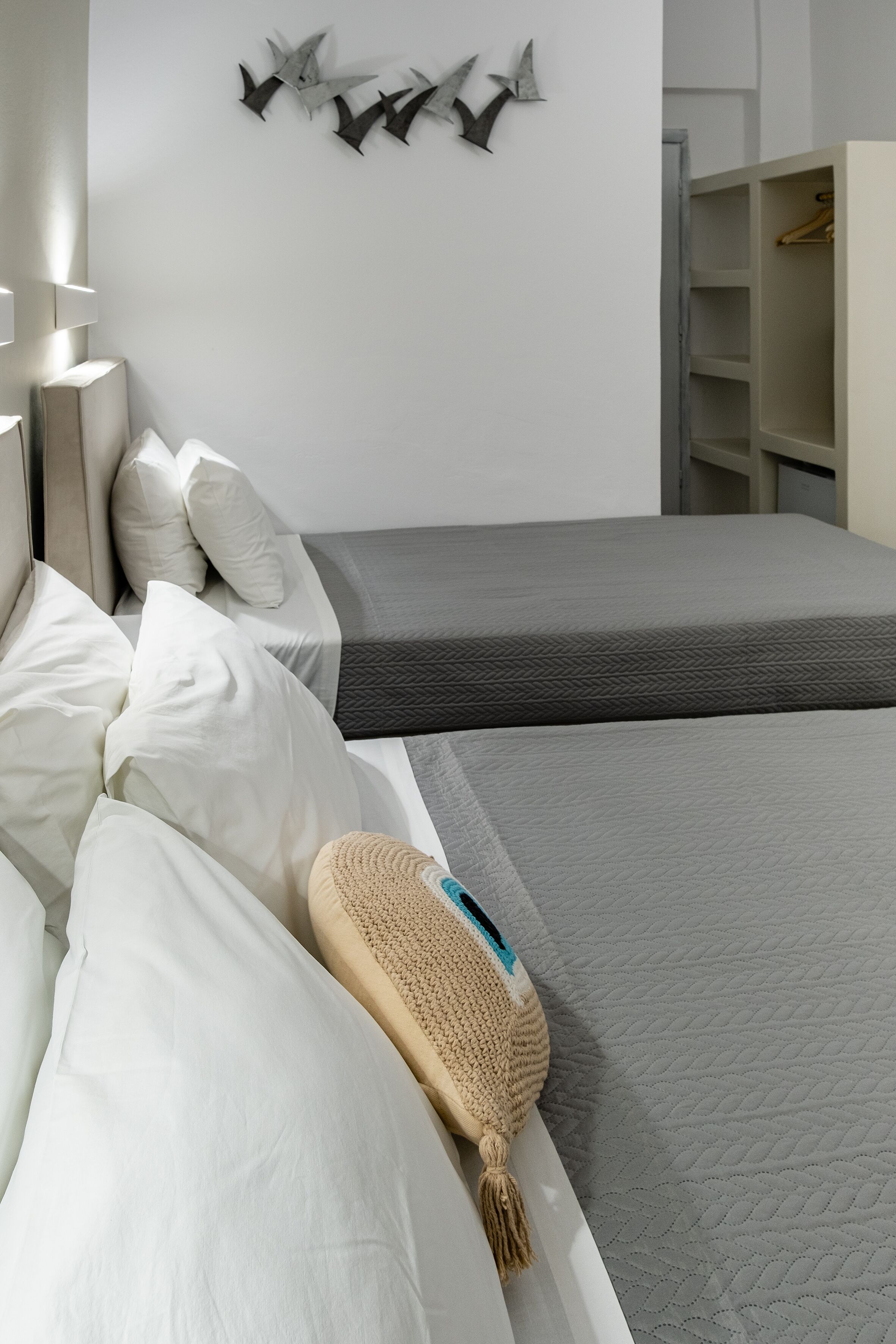 Une chambre moderne avec deux lits, une armoire et une étagère murale agrémentée d’objets décoratifs.