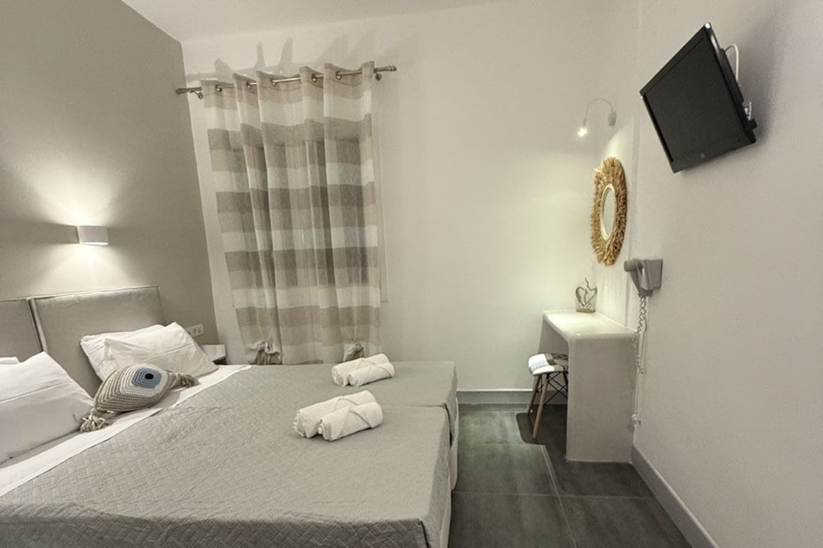 A modern bedroom with a large bed, a bedside table, a small desk, a chair, a television mounted on the wall, and a curtain.