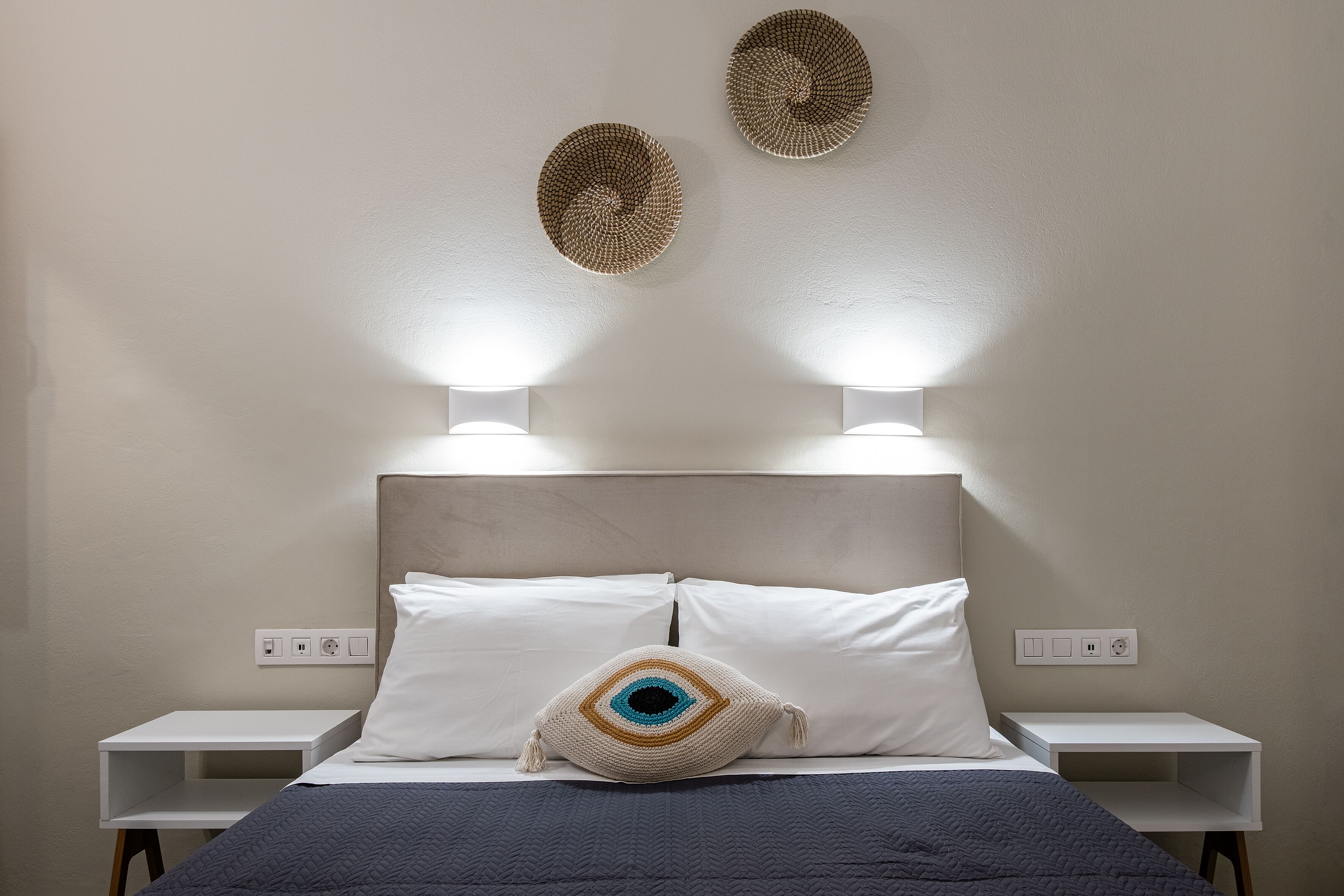 A neatly made bed with a dark quilt, two bedside tables, and wall-mounted lamps.