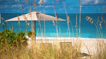 Eine Strandansicht mit einem Strandkorb, zwei Stühlen und hohem Gras im Vordergrund.
