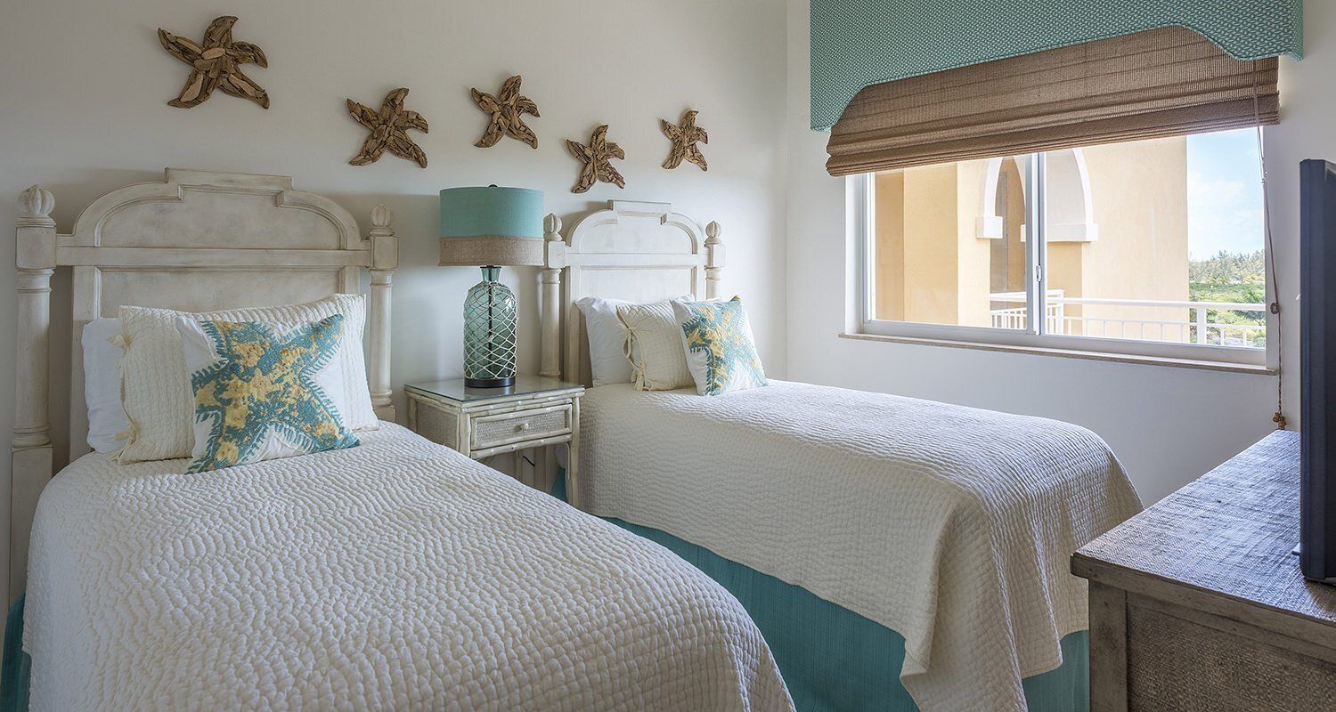 Une chambre avec deux lits, des décorations murales représentant des étoiles de mer, une lampe et une vue sur l’extérieur.