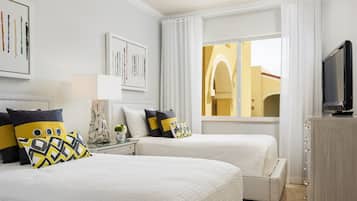 Ein Hotelzimmer mit zwei Betten, einem Fernseher, einem Schreibtisch und einem Fenster mit Vorhängen.