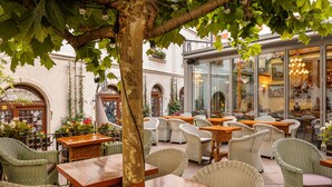 Un café al aire libre con mobiliario de mimbre, un árbol y vistas a la calle.