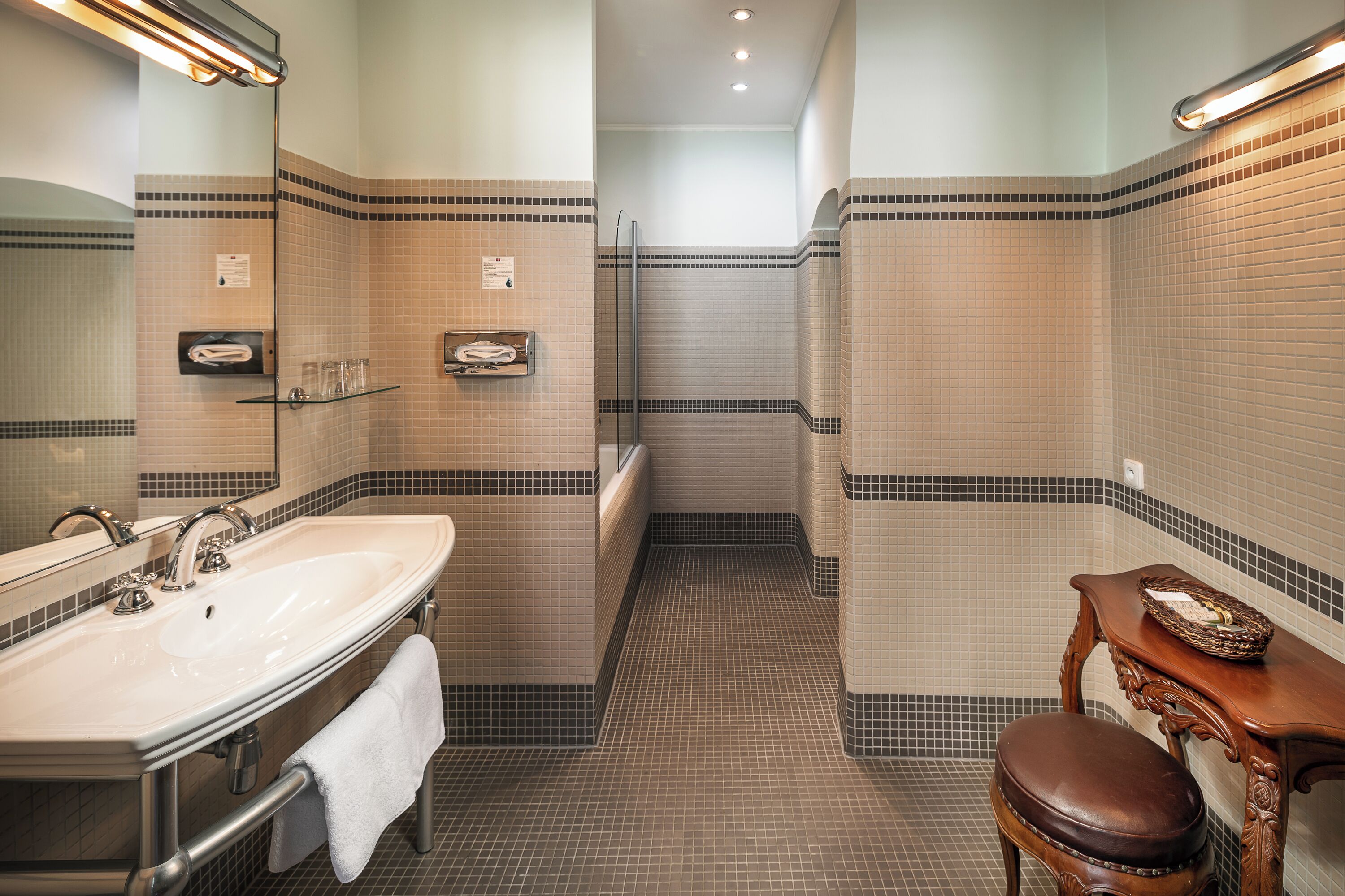 Un baño con un lavamanos grande, un espejo y un banco de madera.