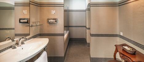 Un baño con un lavamanos grande, un espejo y un banco de madera.