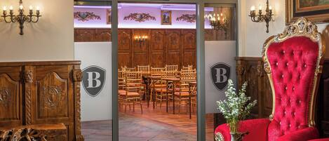 A grand entrance to JILSKA PALACE HALL with ornate wooden doors, a red velvet chair, and a vase with flowers.