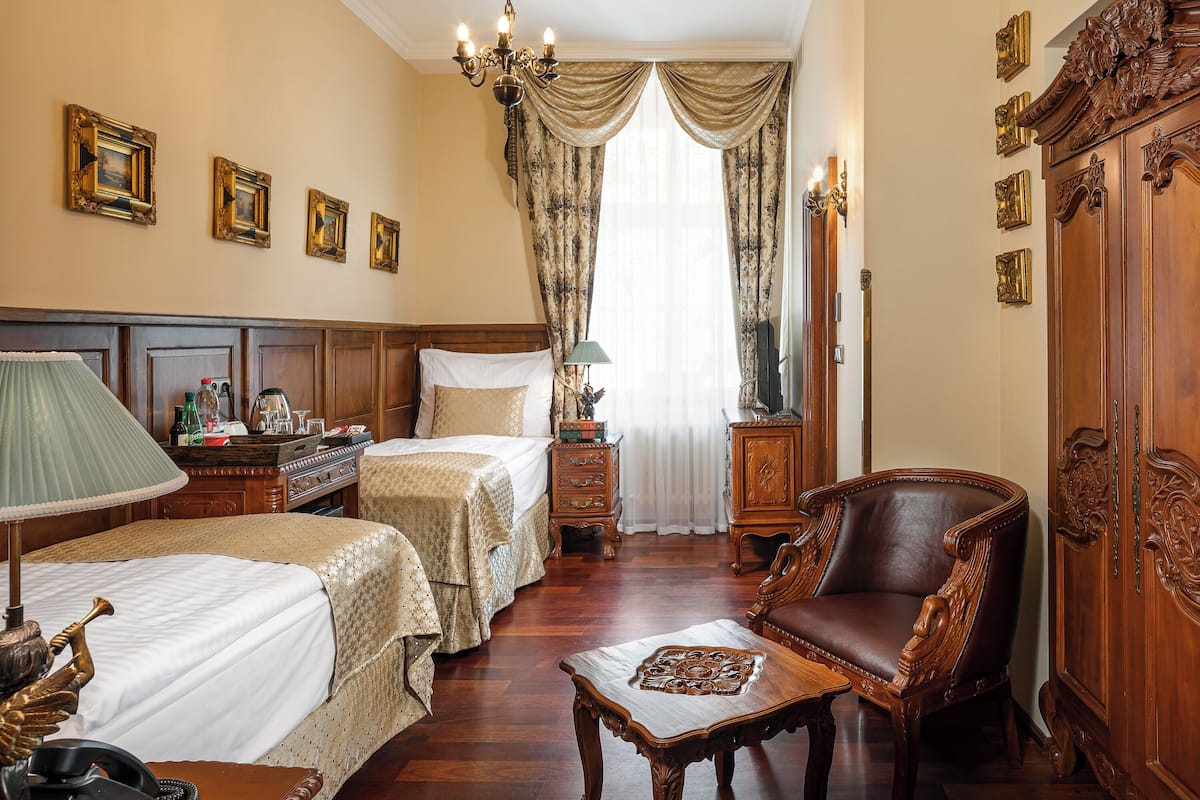 Habitación de hotel con dos camas, una silla de madera, un aparador y un espejo.