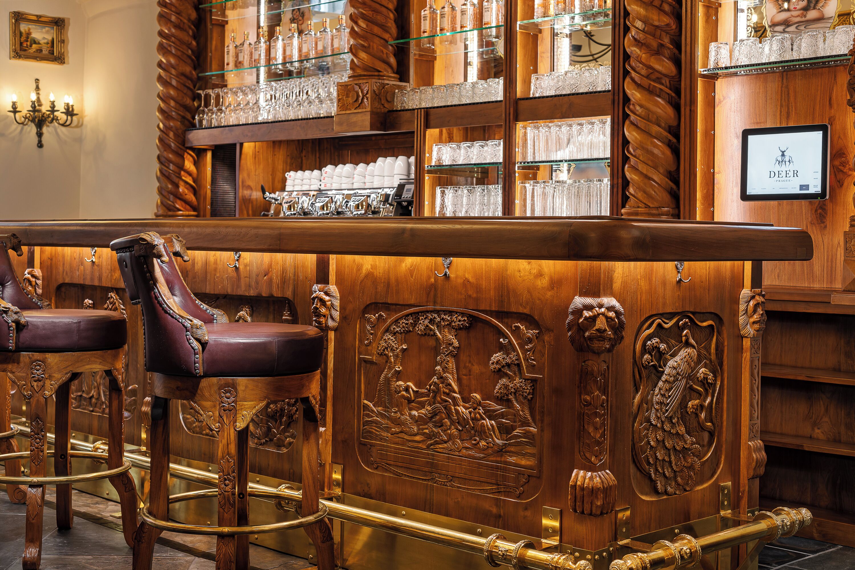 A bar area with wooden bar stools, a polished bar counter, and shelves with glassware and bottles.