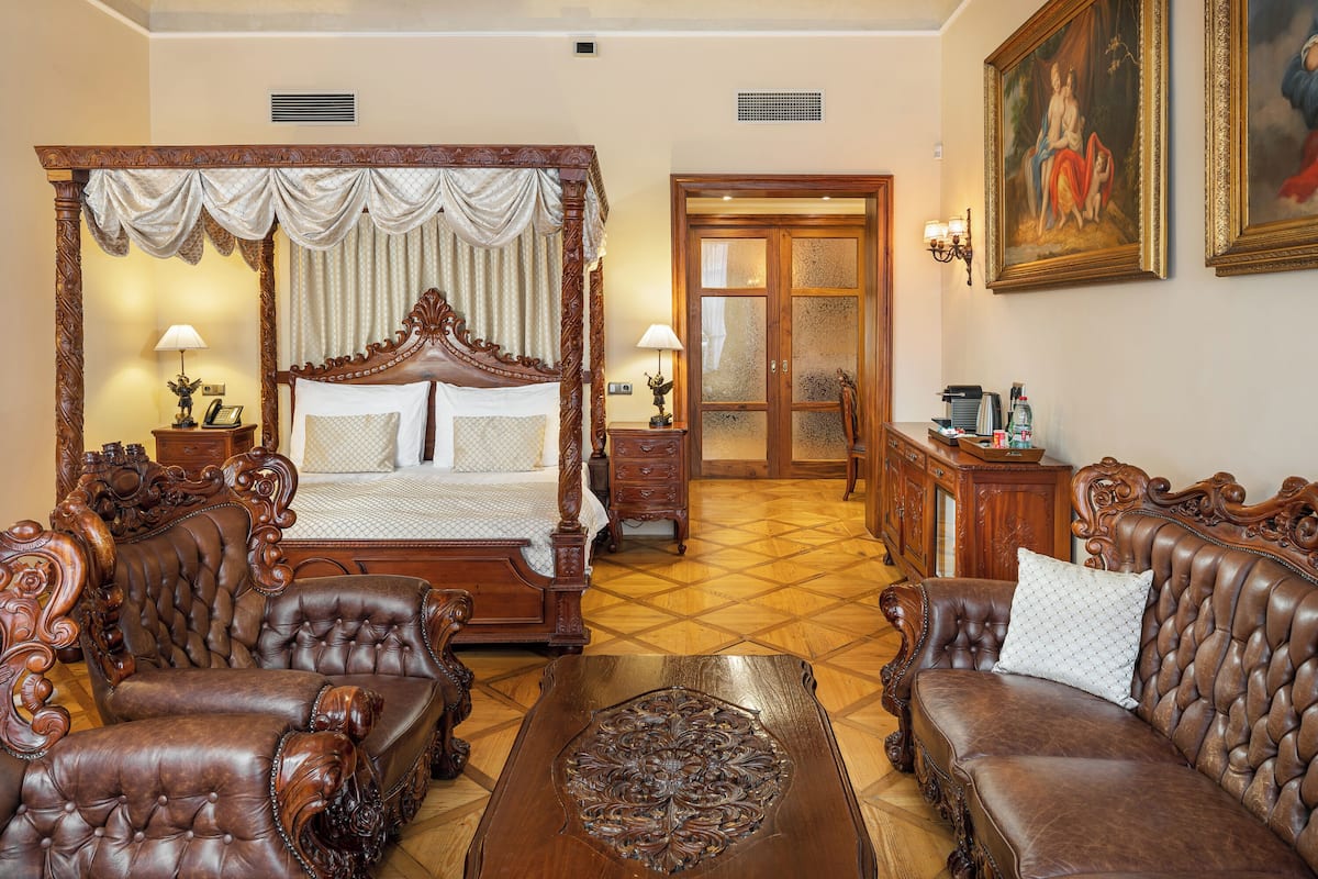 Un dormitorio tradicional con una cama con dosel, dos sillones tapizados, una mesita de centro de madera y una mesita de noche con lámparas.