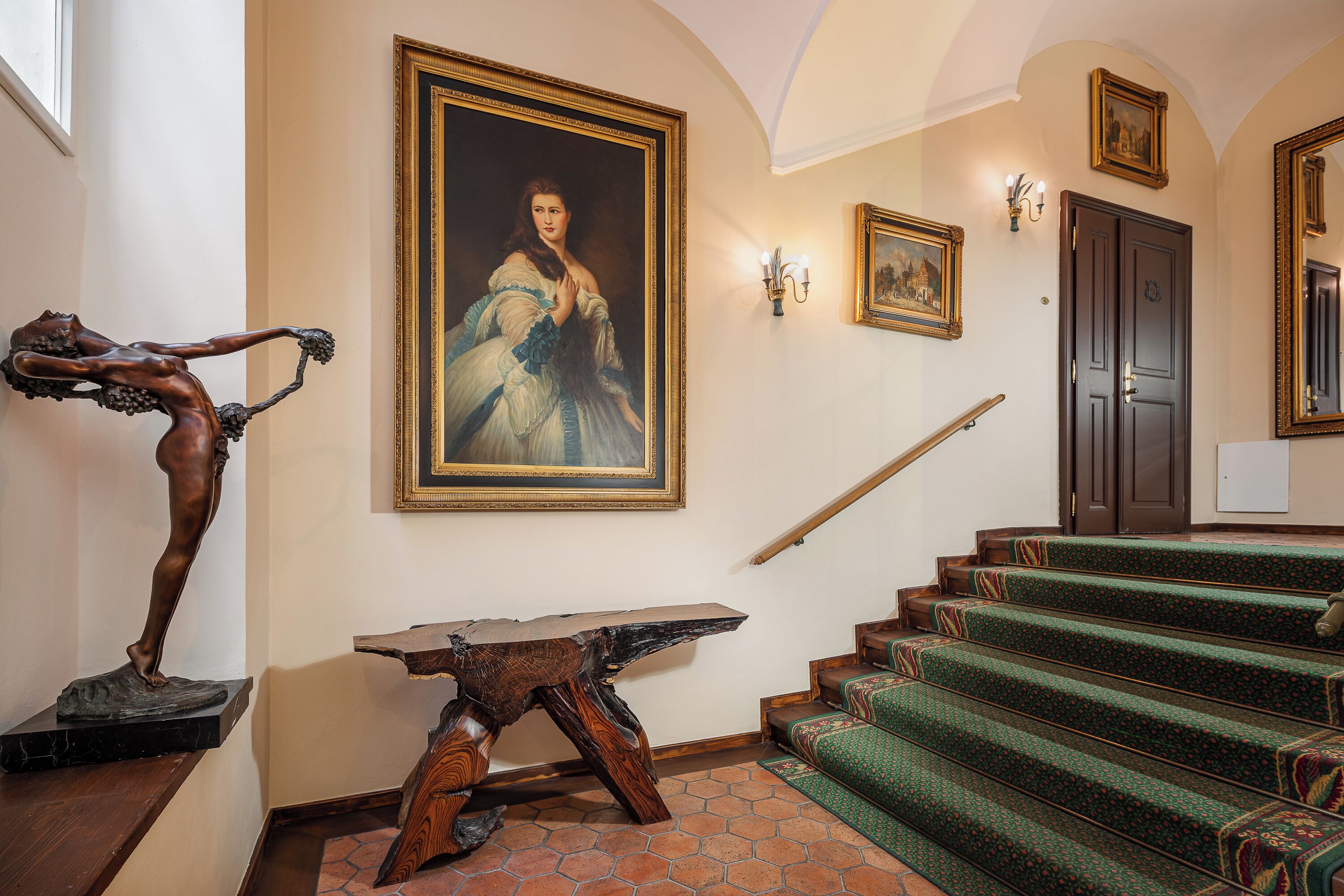A grand staircase with green carpeted steps, a wooden table, and a statue.