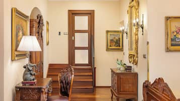 Une pièce avec un plancher en bois, une chaise en bois, un bureau en bois avec une lampe, une commode et une porte dotée d’un panneau en verre dépoli.