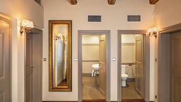 Un pasillo con un espejo grande, dos puertas que dan a un baño y una lámpara en la pared.