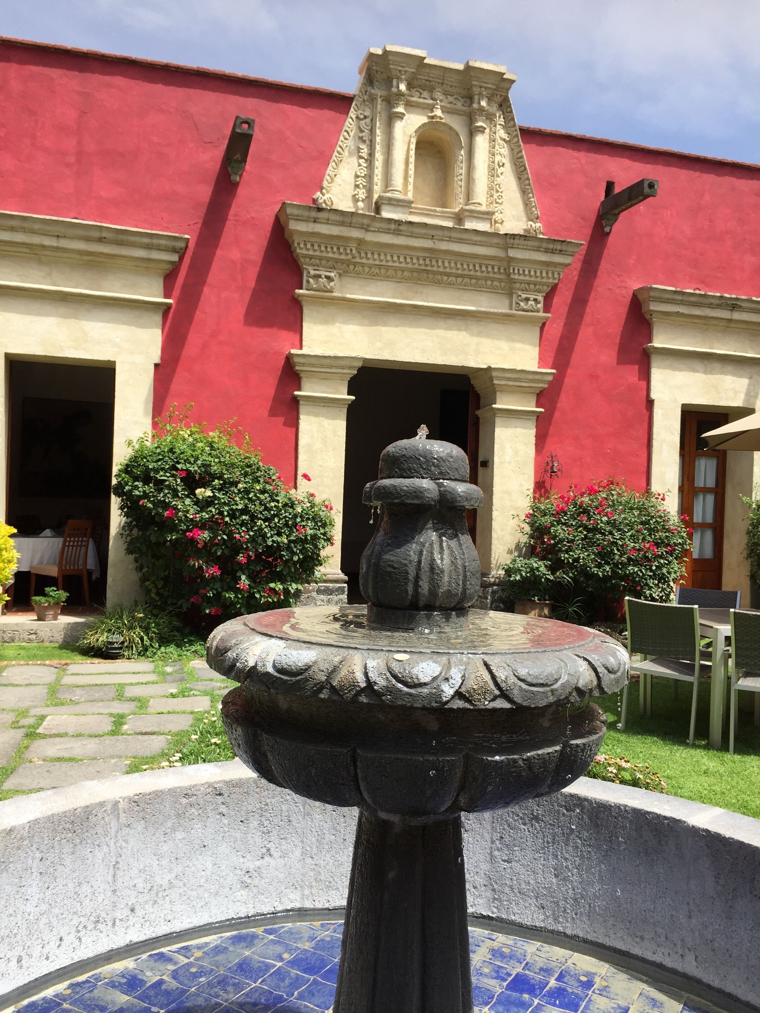 Un patio con una fuente de piedra, paredes rojas y una puerta que da a una habitación con una mesa y sillas.