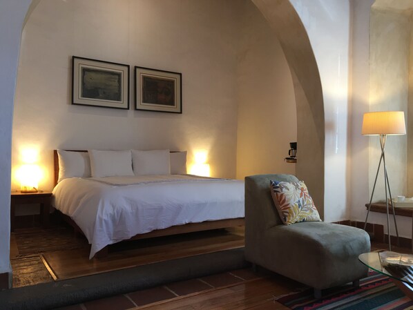 Un dormitorio con una cama, dos lámparas de noche, una silla, una mesita de centro y una lámpara de pie.