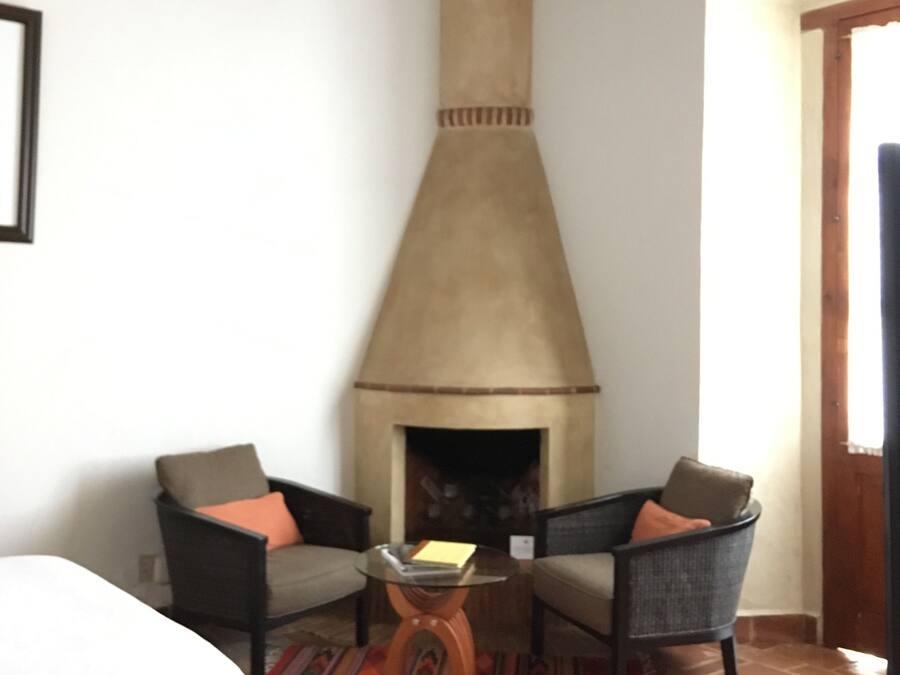 Une pièce avec une cheminée, deux fauteuils, une petite table et un lit.