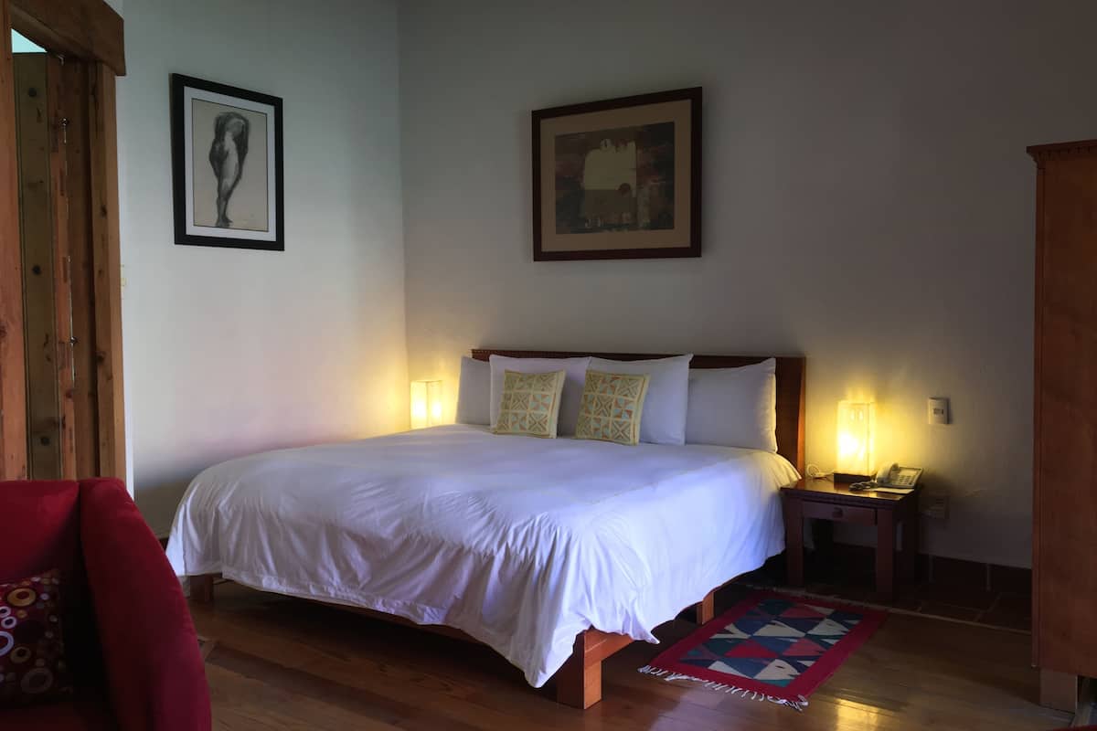 Uma cama bem arrumada com lençóis brancos, duas luminárias de cabeceira e um tapete acolchoado sobre piso de madeira.