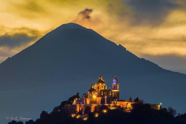 A church with a bell tower and dome, surrounded by a mountainous landscape. - Quinta Luna (San Pedro Cholula)