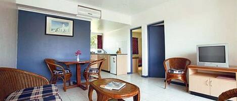 A living room with wicker furniture, a television, and a kitchen area in the background.