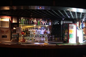 Um balcão de bar com prateleiras cheias de garrafas de bebidas, um caixa registradora e uma geladeira.