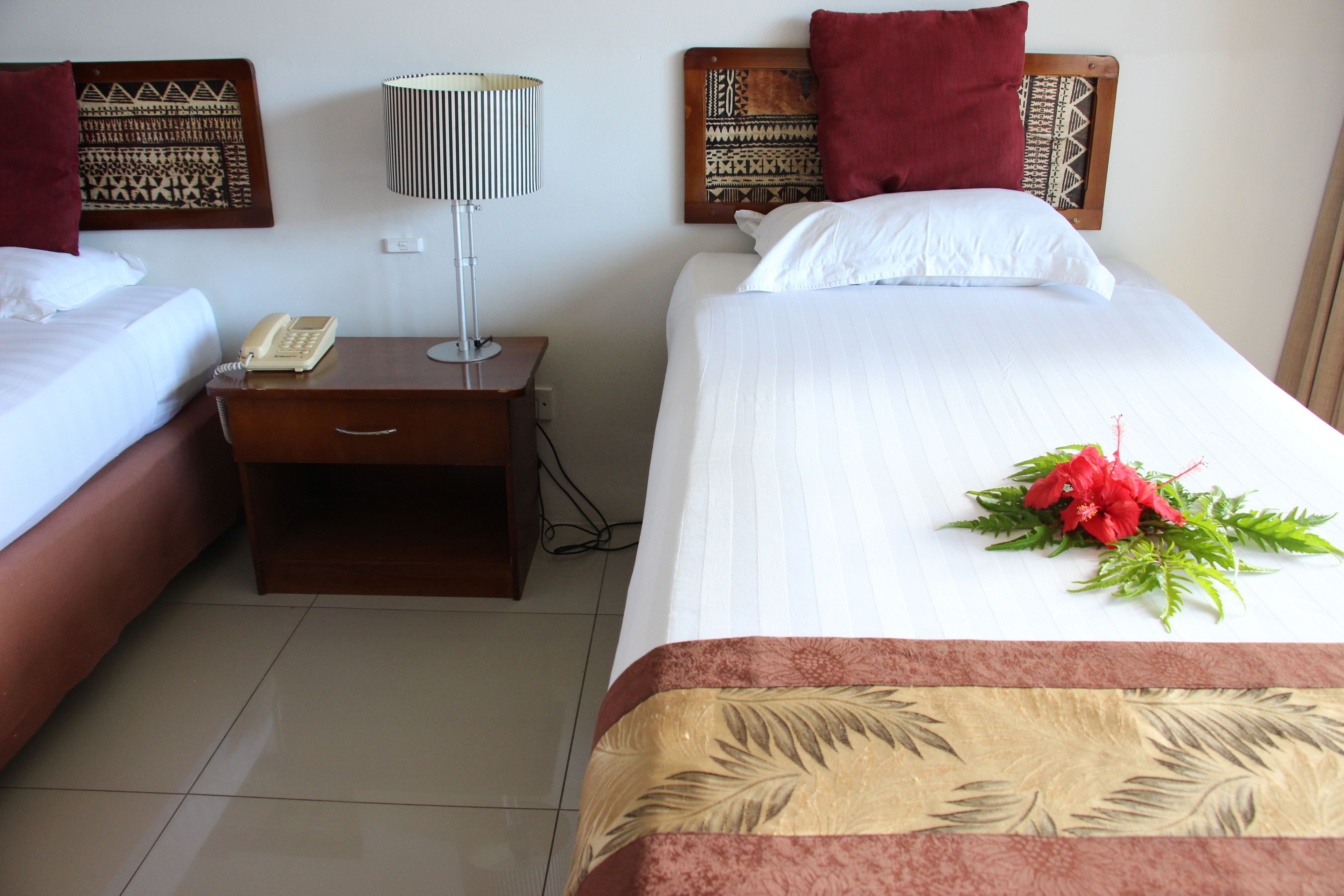A hotel room with two beds, a nightstand with a telephone, a lamp, and a decorative headboard.