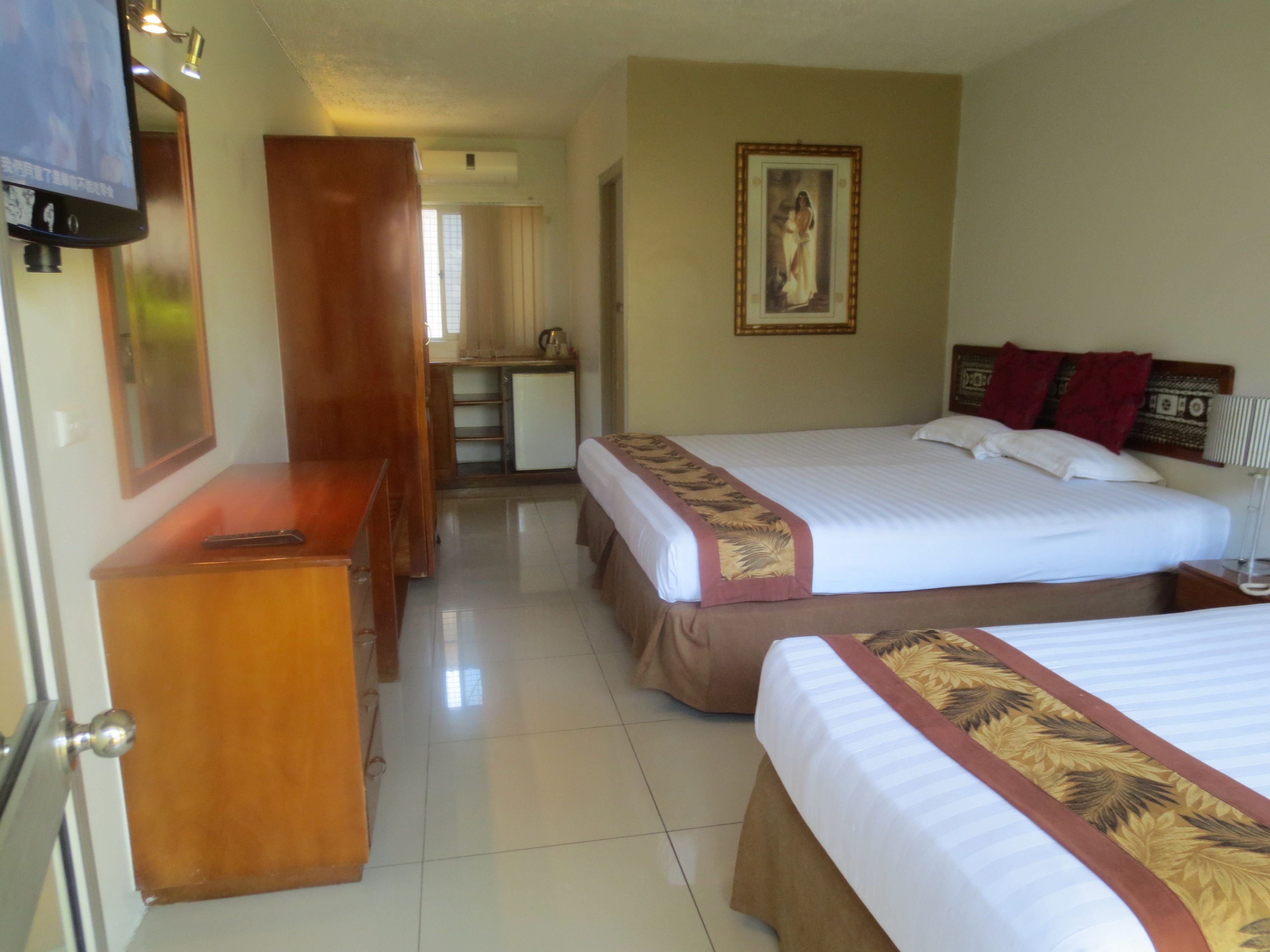 Habitación de hotel con dos camas, un escritorio, un espejo y un televisor.