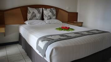 A neatly made bed with a floral arrangement, a wooden headboard, and a bedside table.