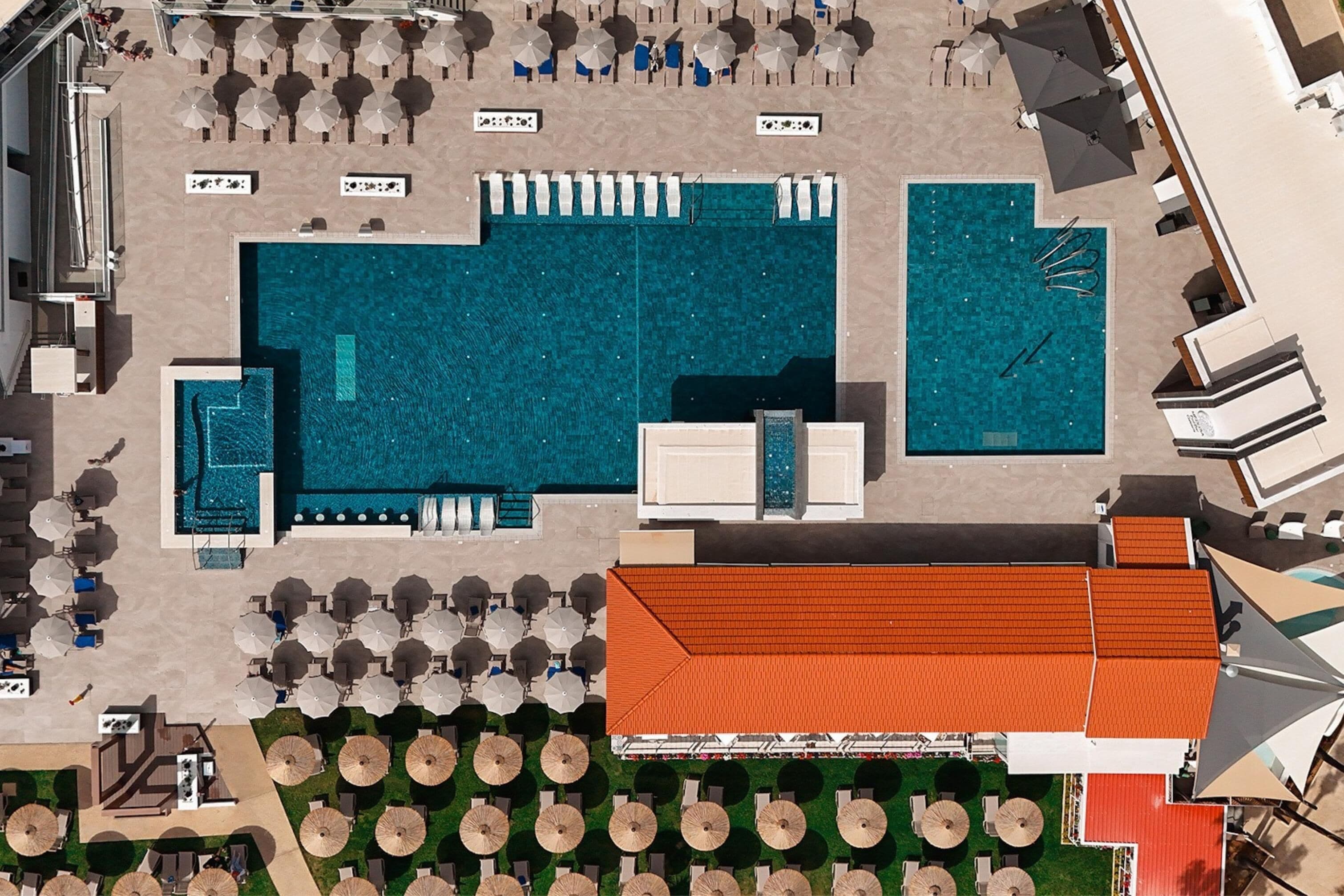 Luchtbeeld van een hotel met meerdere zwembaden, ligbedden en parasols.