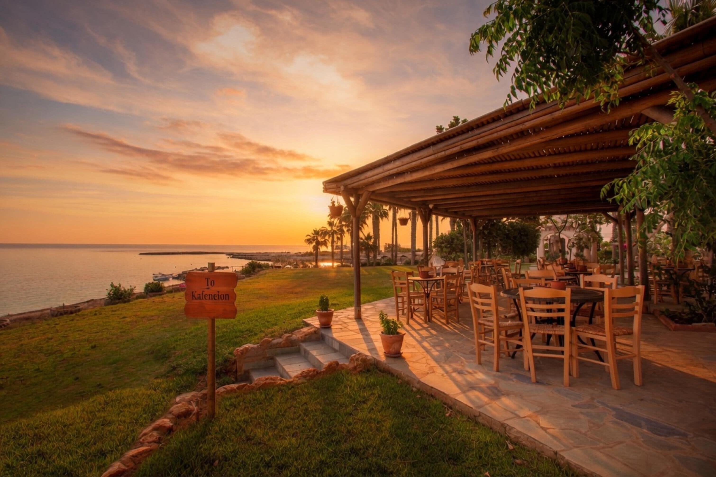 Een terras met buitenmeubilair, een bord en uitzicht op zee bij zonsondergang.
