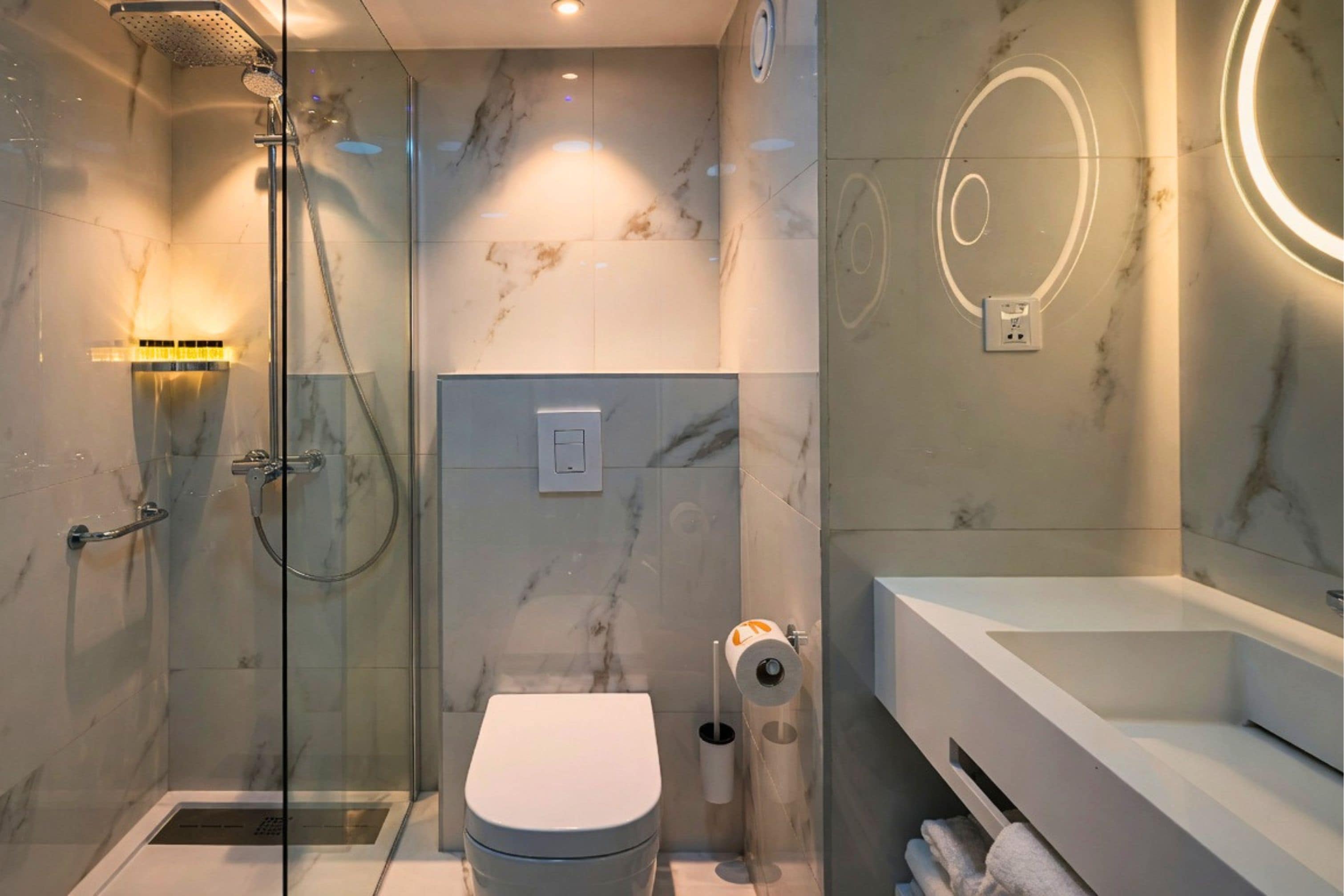 Un baño moderno con ducha envuelta en vidrio, inodoro y lavamanos con espejo.