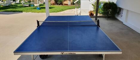A ping pong table with a net, set up outdoors with a view of a pool and palm trees.
