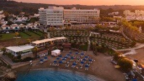 A coastal resort with a beach area, lounge chairs, and a large building with multiple floors. - Cavo Maris Beach Hotel (Paralimni)