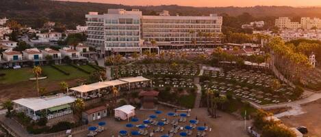 A coastal resort with a beach area, lounge chairs, and a large building with multiple floors.
