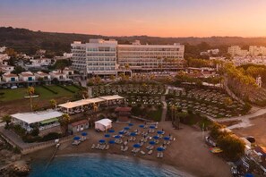 A coastal resort with a beach area, lounge chairs, and a large building with multiple floors. - Cavo Maris Beach Hotel (Paralimni)