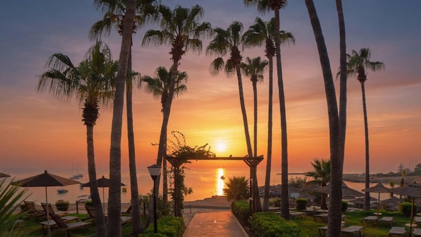 A sunset view with palm trees and beach umbrellas. - Cavo Maris Beach Hotel (Paralimni)
