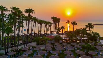 Un resort con tumbonas y sombrillas, palmeras y vista al atardecer.