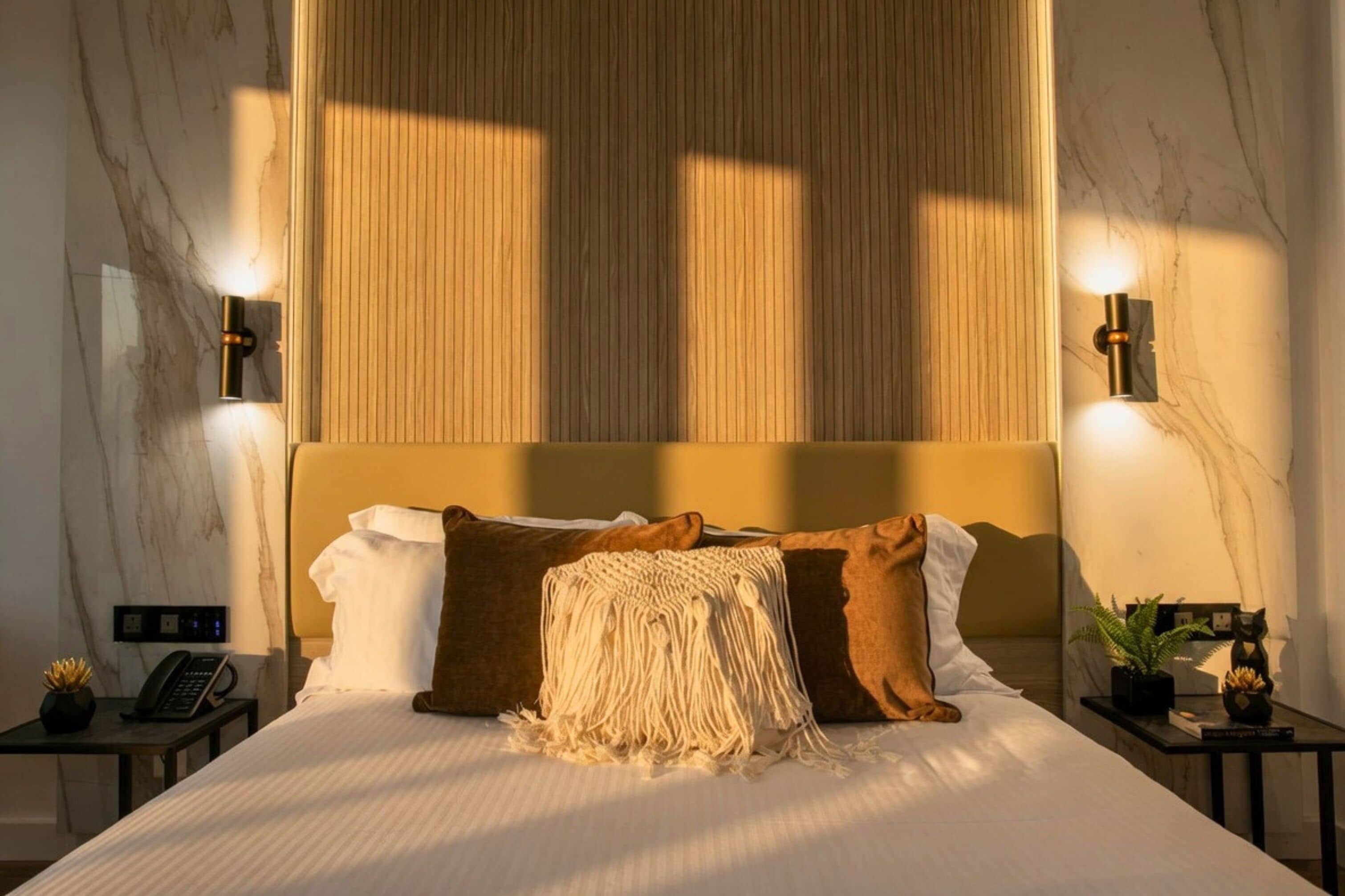 A hotel room with a bed, a nightstand with a phone, a lamp, and a small table with a plant.
