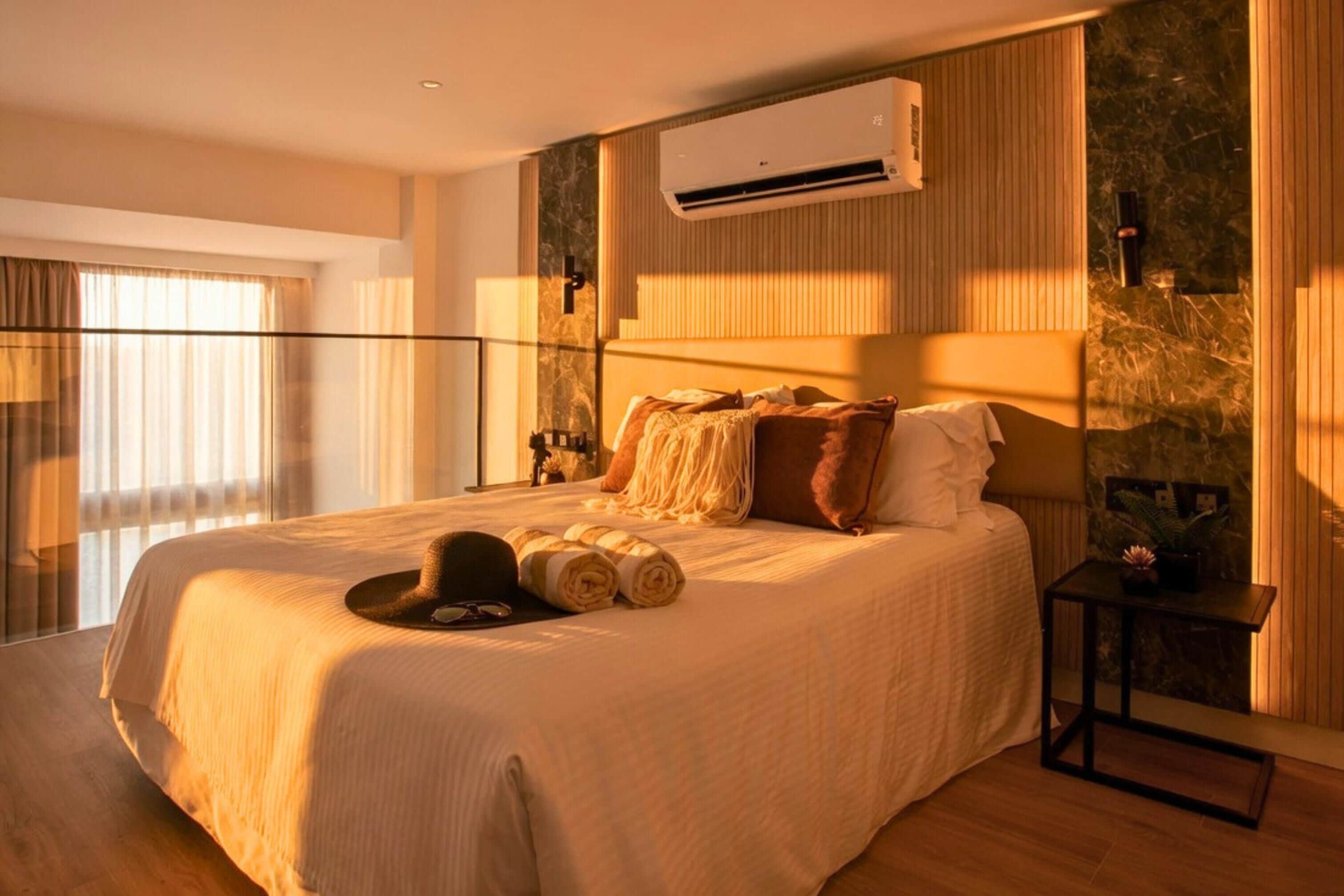 A hotel room with a large bed, an air conditioning unit, a nightstand, and a view of the outdoors.