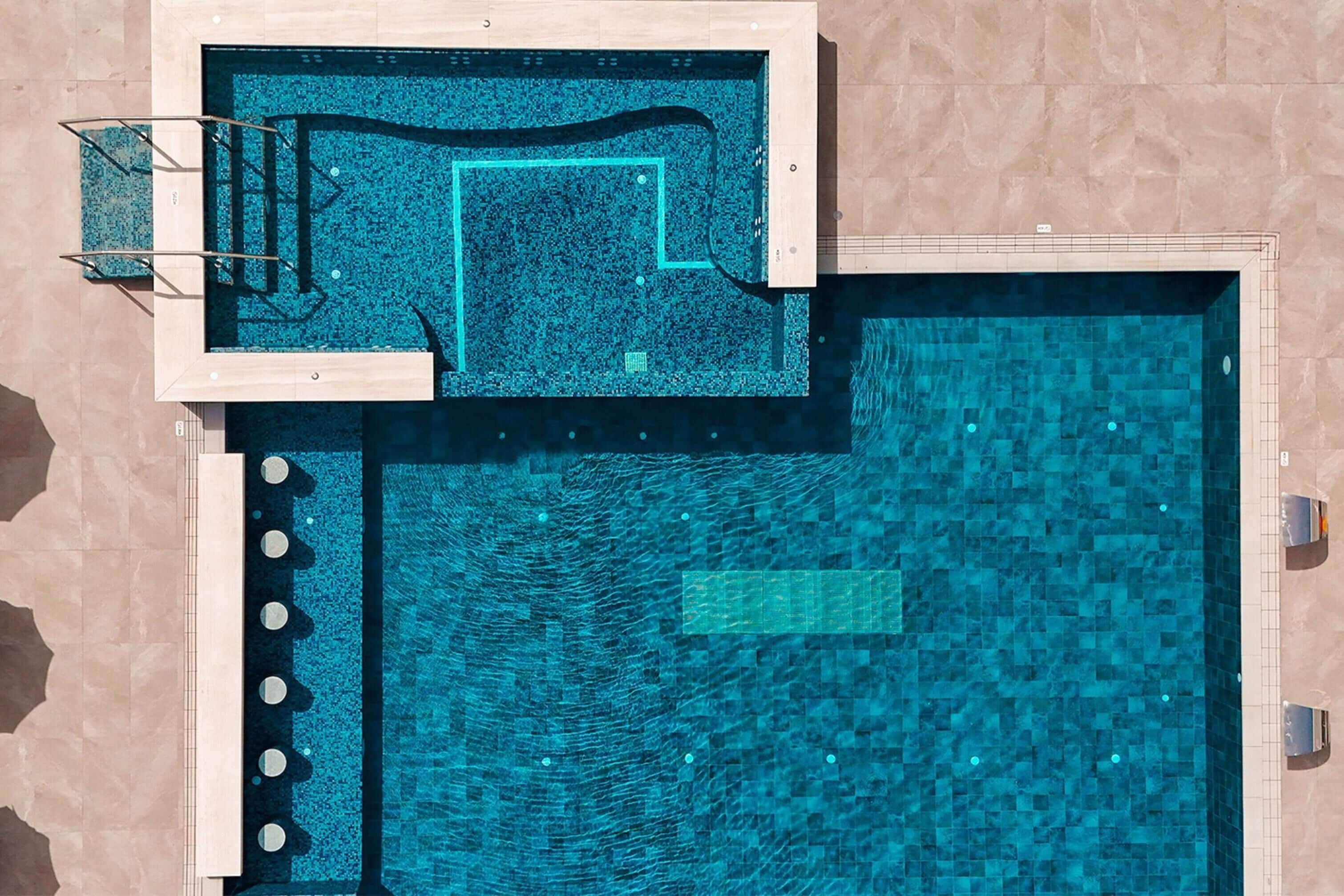 Una piscina rectangular grande con zona de terraza empavedada y una sección separada con un diseño de baldosas diferente.